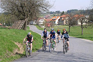 Cyklistika ve Žďárských vrších, pět cyklistů vyjíždějících kopec od vesnice.